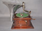 a silver gramphone on a wooden stand with a green plate