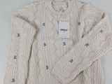 Le pull est blanc et comporte des boutons bleus.