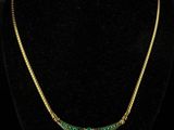 a gold and emerald necklace on a black mannequin