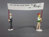 two figurines of a man and a woman holding a sign