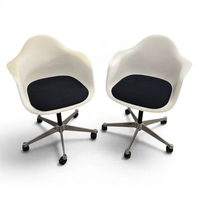pair of white chairs with black cushions and wheels on a white surface
