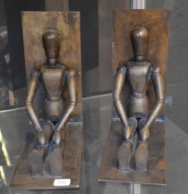 deux statues en bronze représentant une personne assise sur un banc