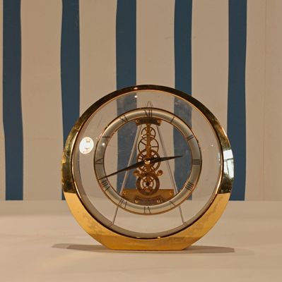 a gold clock sitting on a table with a blue and white striped wall behind it