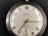 a silver pocket watch hanging on a black wall