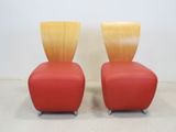 pair of red leather chairs with wooden backrests on casteors