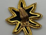 a close up of a gold and black brooch with a praying hand on it