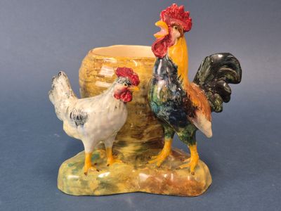 deux coqs en céramique posés sur un rocher à côté d'un vase