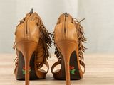 tan fringed heels on a wooden table with a white curtain in the background