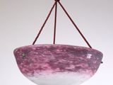 un bol en verre violet et blanc suspendu à une corde sur un mur blanc