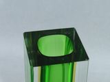 a green glass vase with a black base on a white surface