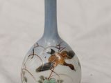a small vase with a bird on it sitting on a white surface