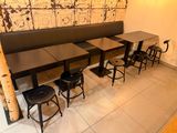 Dans un restaurant, des tables et des tabourets sont alignés, avec un mur en bois en arrière-plan.