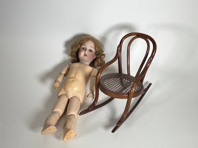 une poupée assise à côté d'un fauteuil à bascule sur une surface blanche