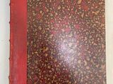 an old book with a red cover sitting on top of a white table