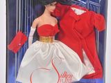 La poupée se trouve dans la boîte, vêtue d'un manteau rouge et d'une robe blanche.