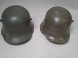 pair of wwii era german steel helmets on a white surface