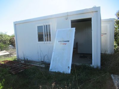un petit bâtiment blanc dont la porte est ouverte, au milieu de l'herbe