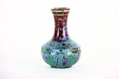 un vase violet et vert posé sur une surface blanche