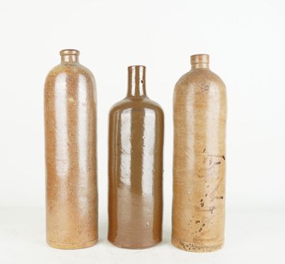 trois bouteilles en verre brun posées les unes à côté des autres sur une surface blanche
