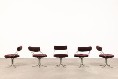 four red chairs sitting in a row on top of a cement floor