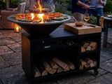 two people standing around a fire pit with food on it
