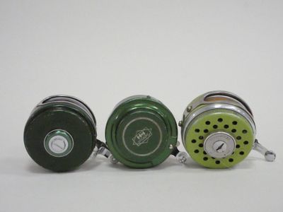 three different colors of fishing reels on a white surface
