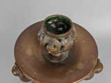 a gold candle holder with a green glass on top of it