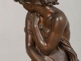 an antique bronze statue of a woman sitting on a rock with her hands on her face