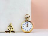 a gold pocket watch sitting next to a key on a marble block