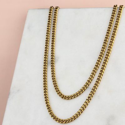 a gold chain necklace on a marble slab with a pink background