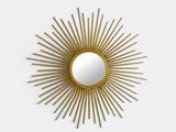 a close up of a gold sunburst mirror on a white wall