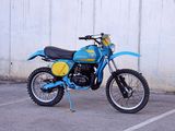 a blue motorcycle parked in a parking lot next to a white wall