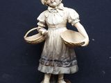 une statue représentant une jeune fille avec un panier, assise sur un rocher