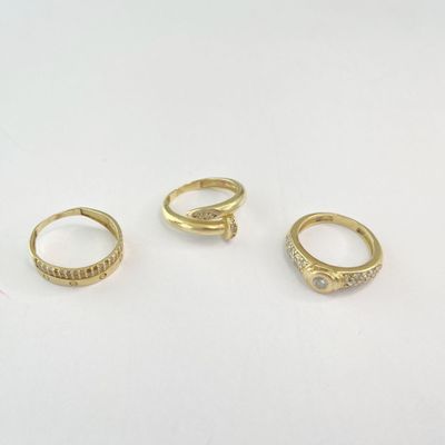 trois bagues en or serties de diamants, posées sur une surface blanche