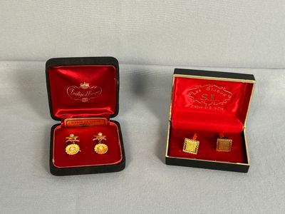 deux paires de boucles d'oreilles en or dans un écrin rouge posé sur une surface blanche