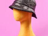 chapeau de pêcheur en cuir noir posé sur une tête de mannequin, sur fond rose