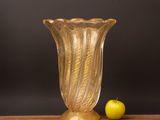 yellow glass vase sitting on top of a wooden table next to an apple