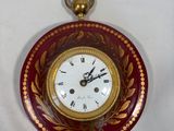 a red and gold clock hanging on a white wall