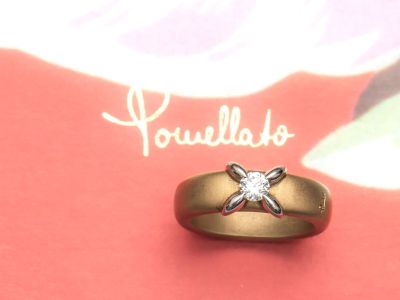 une bague en or sertie d'un diamant, posée sur un fond rose