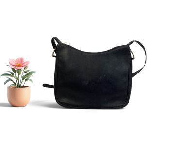 un petit sac à main noir posé à côté d'une plante en pot sur une surface blanche