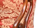 a red and gold upholstered chair with a wooden arm
