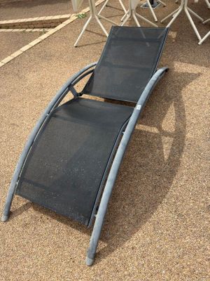 a black lounge chair sitting on the ground in front of a table and chairs