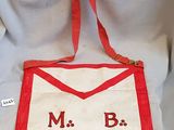 un tablier rouge et blanc sur lequel figurent les lettres « m b »