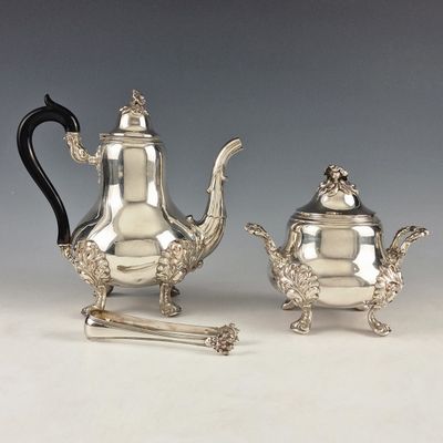 two silver teapots and a sugar shaker on a table
