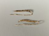 two gold hair pins with a long tail sitting on top of a white surface