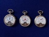 trois montres de poche en argent posées côte à côte sur une surface bleue