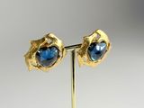 a pair of gold earrings with blue stones on a stand