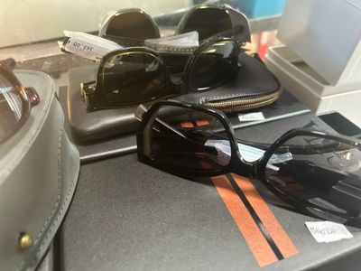 une paire de lunettes de soleil noires posée sur une valise, à côté d'une autre paire de lunettes de soleil noires