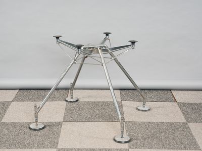 une petite table en métal à quatre pieds posée sur un sol en damier