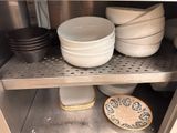 several bowls and plates are stacked on a metal shelf in a kitchen